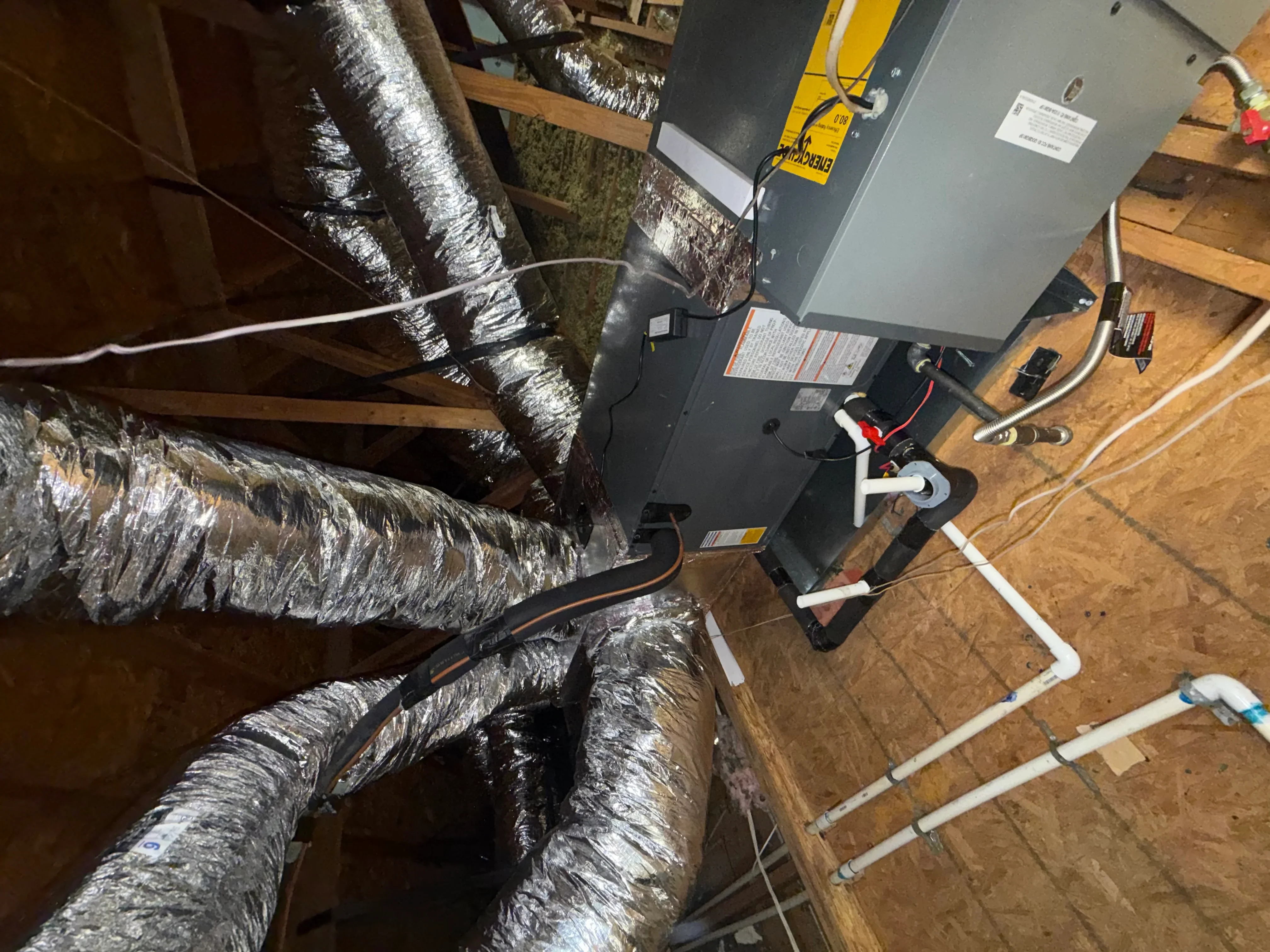 HVAC installation with insulated flex ducts, air handler unit, and PVC drain lines on wooden framing